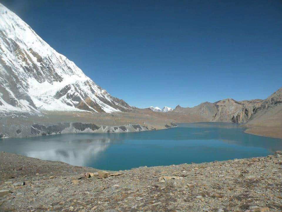Tilicho Lake nestled in the high Himalayas with snow-capped peaks and blue water under a clear sky.