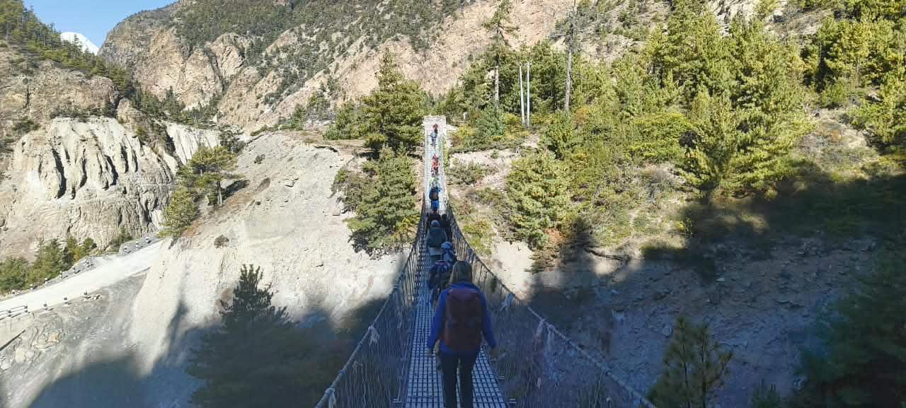 Group of hikers crossing a suspension bridge on the Annapurna Circuit trek in Nepal with mountain scenery