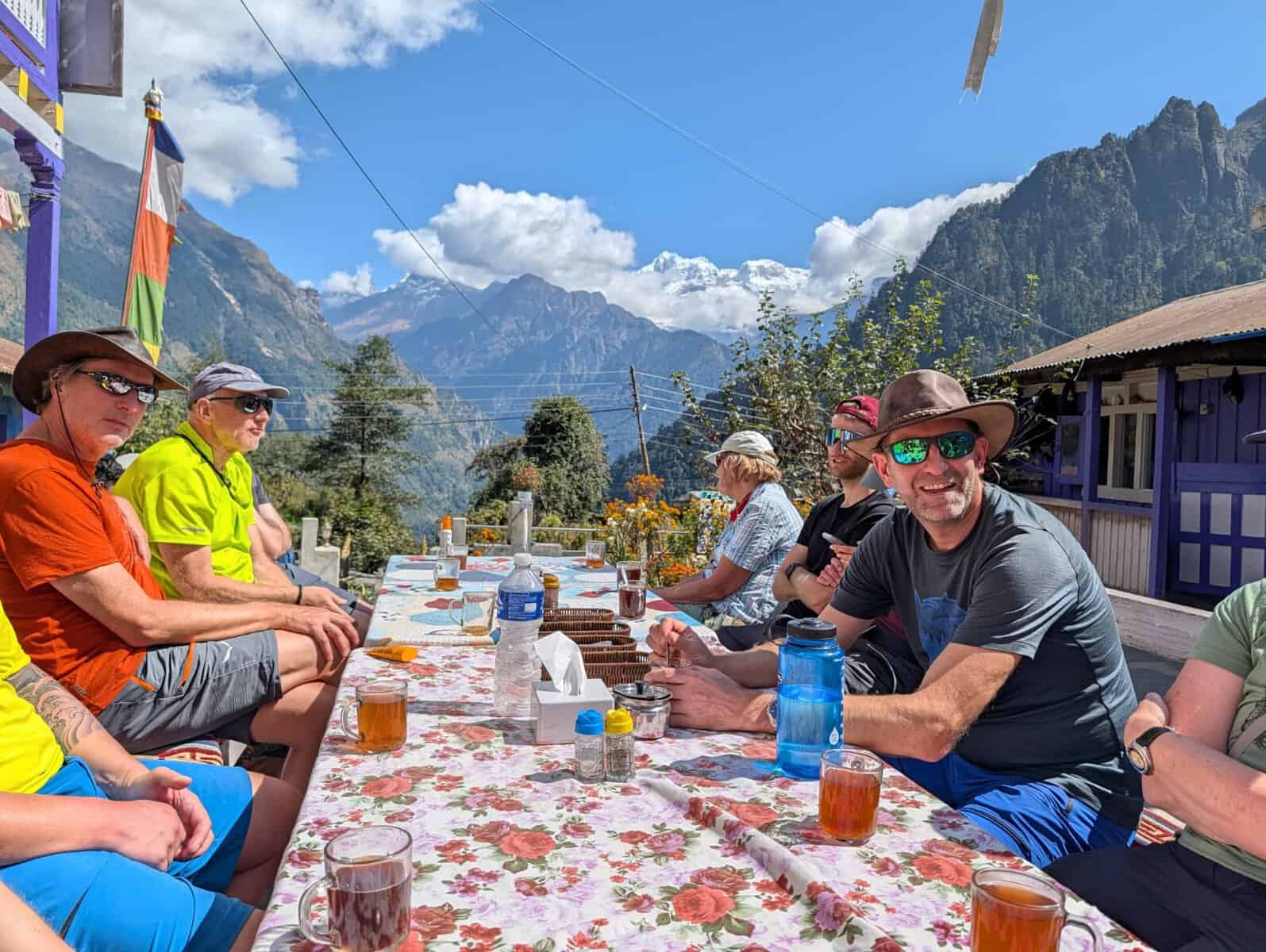 Trekkers enjoying lunch on a sunny outdoor patio with scenic Himalayan mountain views in Nepal.