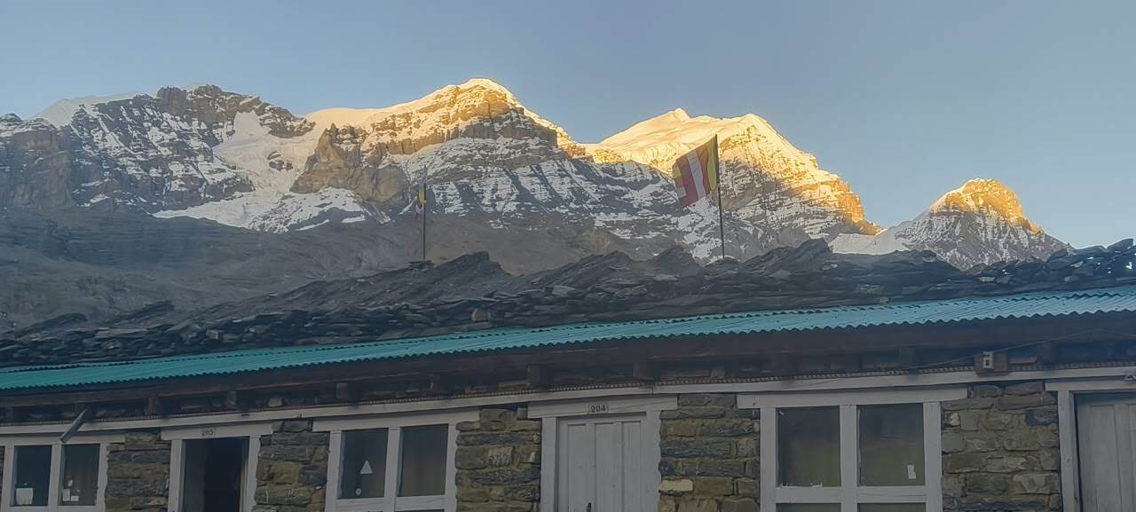 Sunrise over snow-capped Himalayan mountains with a traditional stone lodge in the foreground