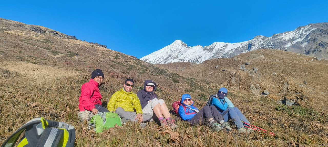Hikers resting on a mountain slope with snow-capped peaks in the background during a trek