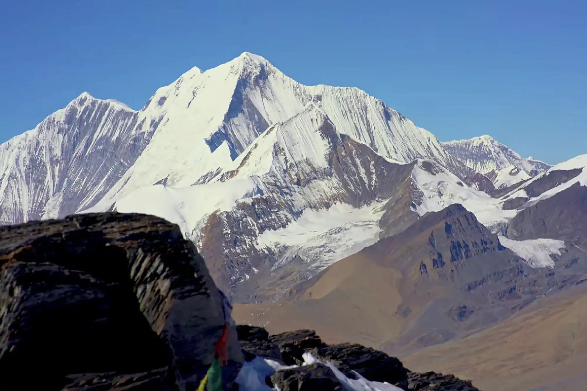 Snow-covered Himalayan mountain peaks rising under a clear blue sky viewed from a rocky ridge