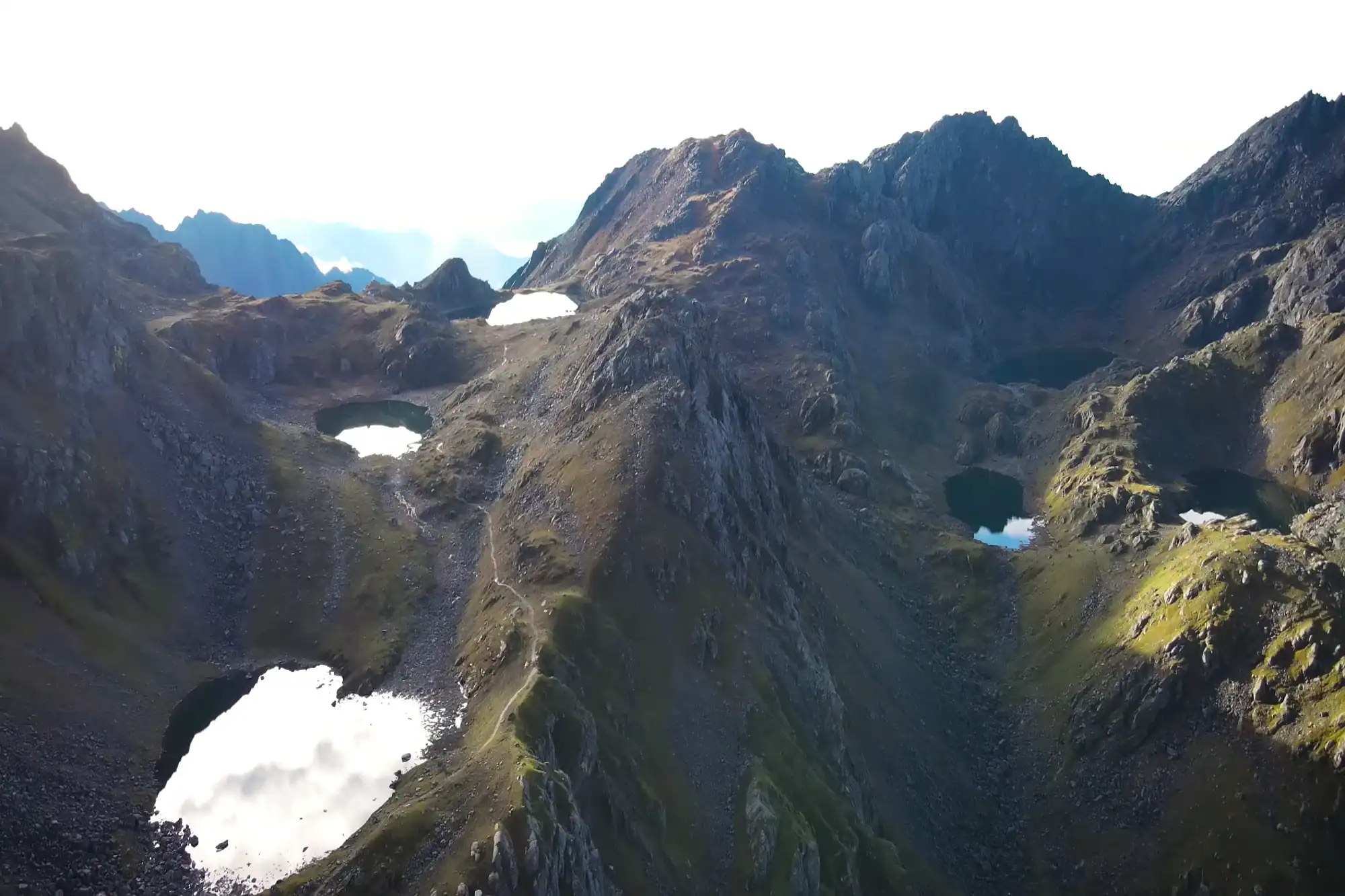 Aerial view of rugged mountain peaks and reflecting alpine lakes along a high-altitude hiking trail ridge.
