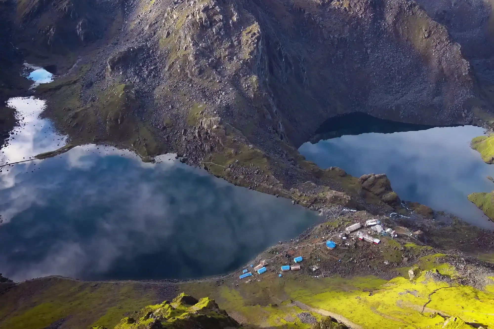 Aerial view of Gosainkunda alpine lakes reflecting clouds surrounded by rugged Himalayan mountains in Nepal.