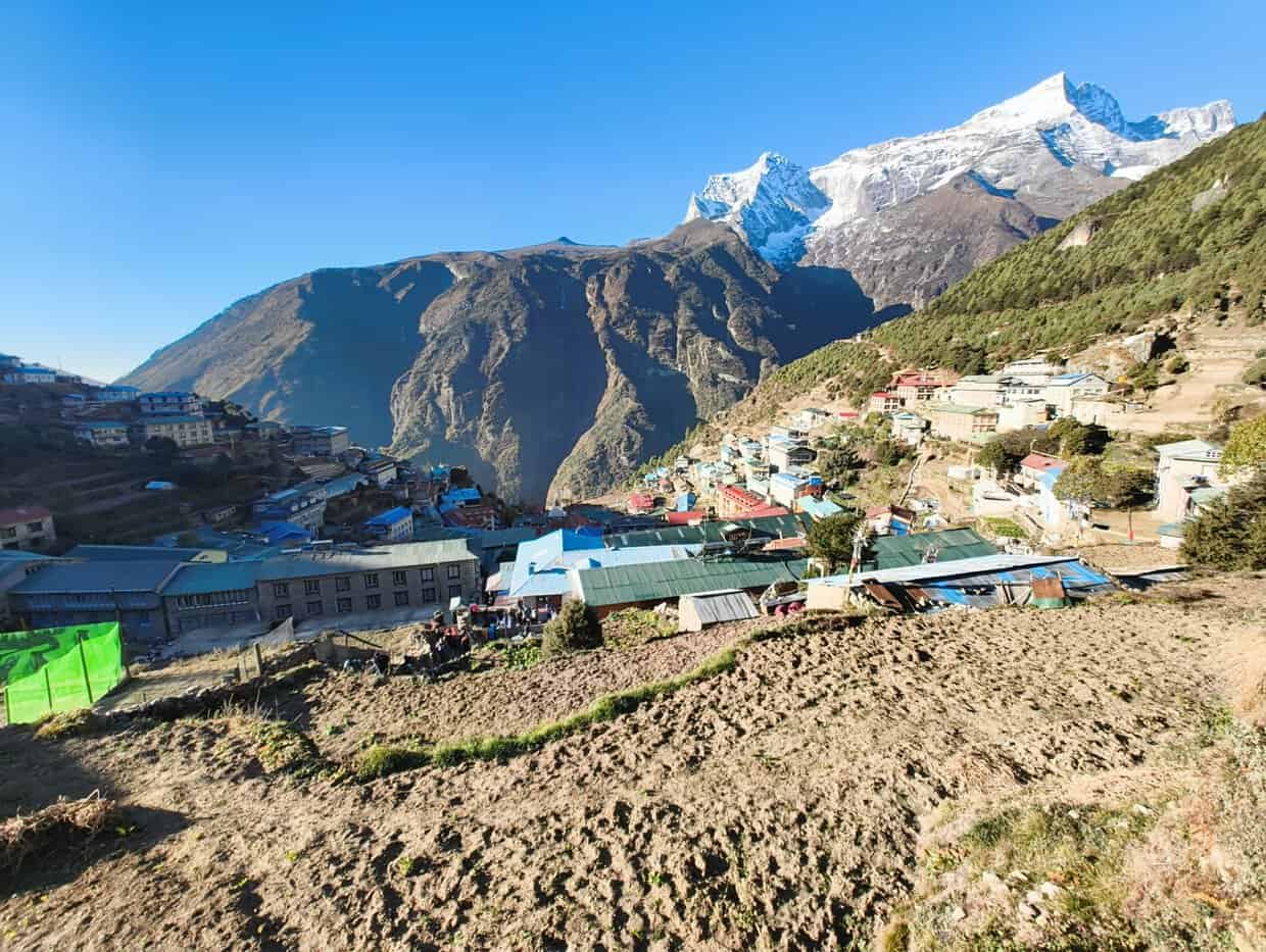Namche Bazaar village nestled in the Himalayas with snow-capped mountain peaks and clear blue sky in Nepal