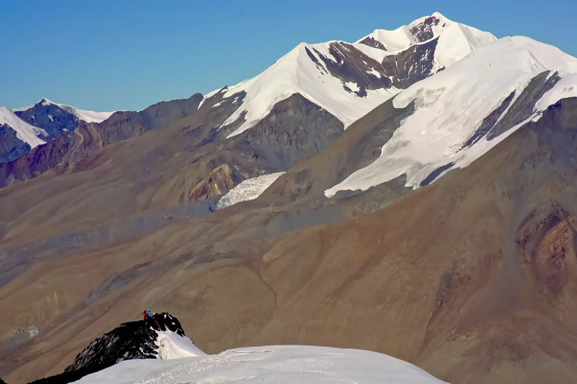 Climbers on a snowy ridge overlooking majestic snow-capped mountain peaks and glaciers