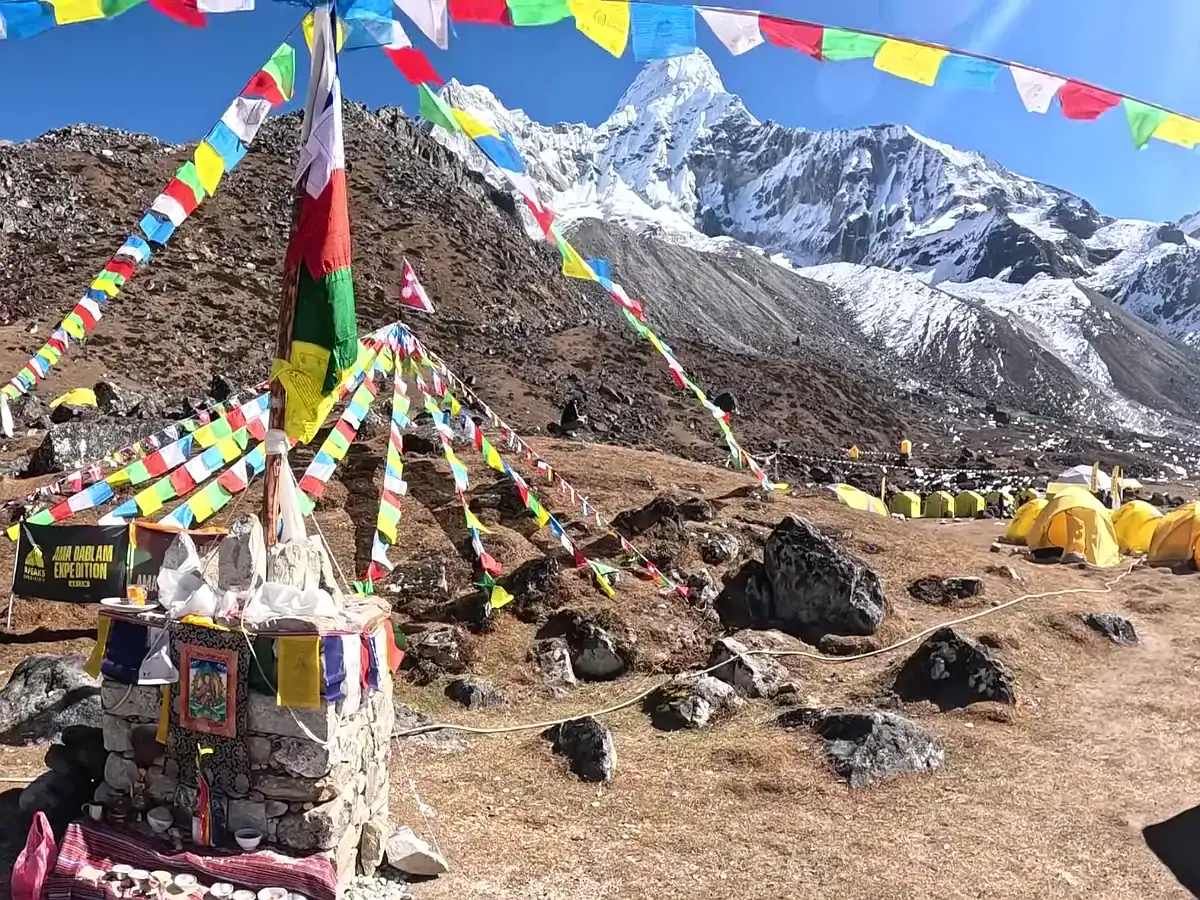 Colorful prayer flags at Ama Dablam base camp with yellow expedition tents and snow-capped Himalayan mountains