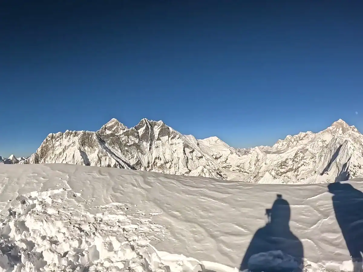 Panoramic view of snow-covered Himalayan peaks with a mountaineer shadow on a snowy ridge