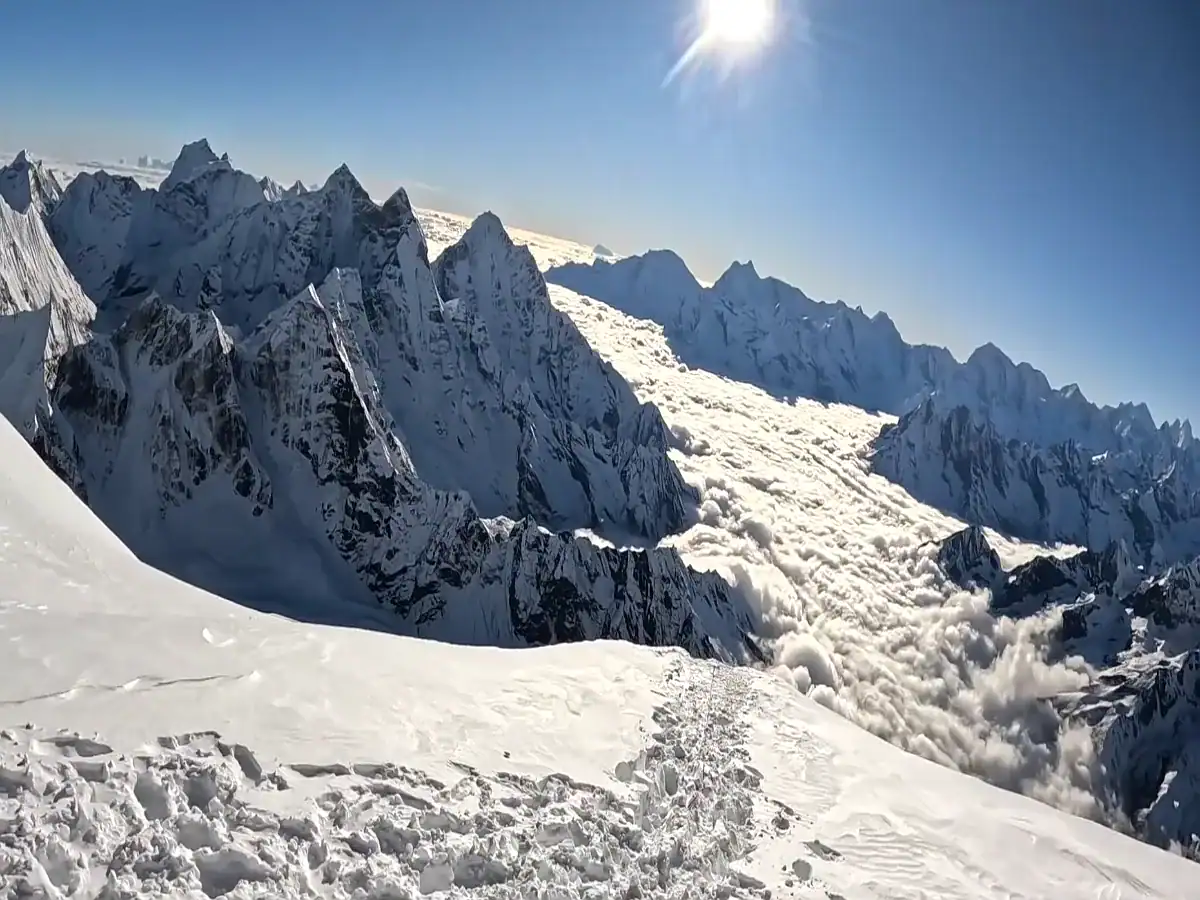 Snowy mountain ridge trail overlooking rugged peaks and a sea of clouds under a bright sun