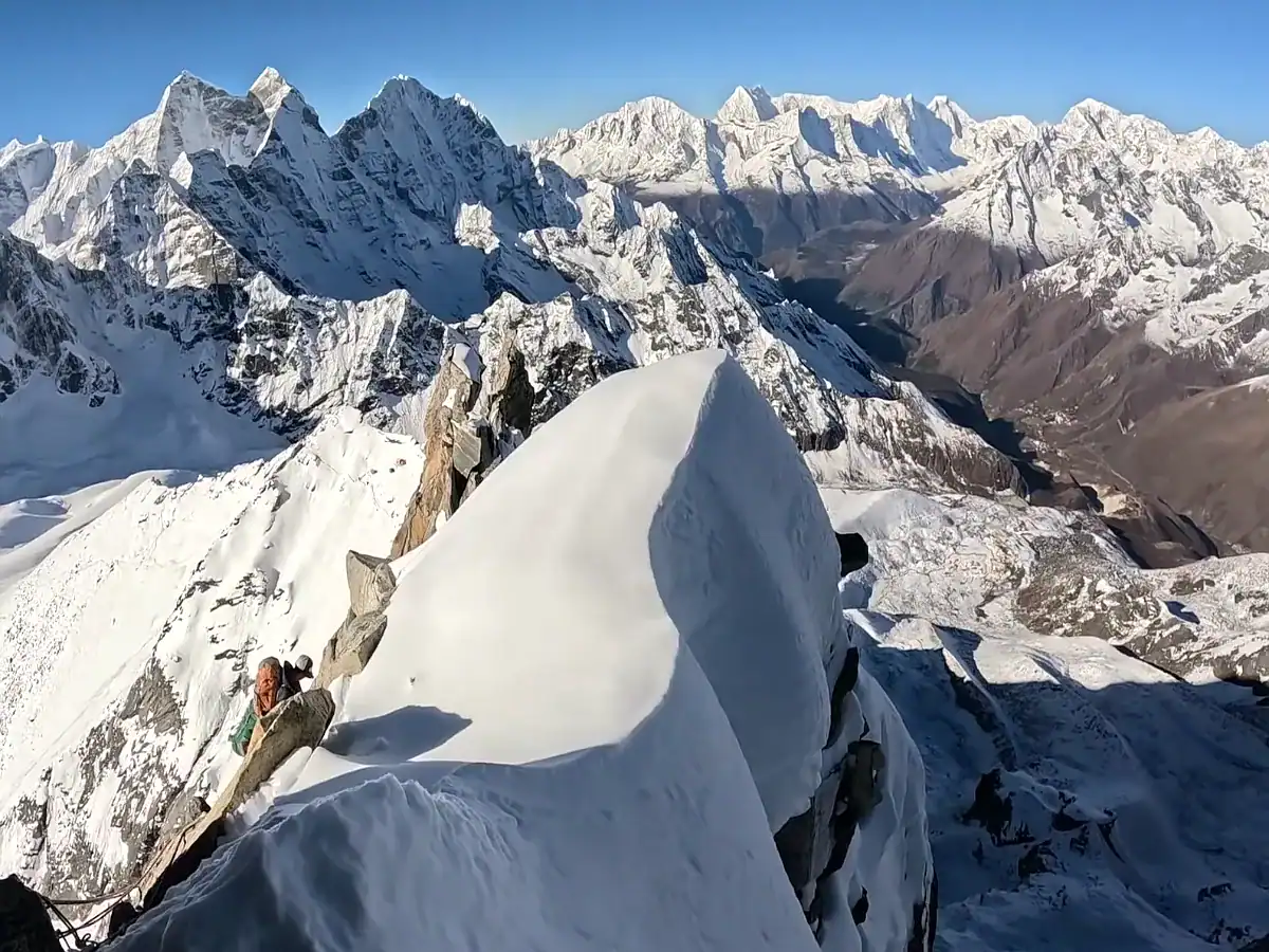 Mountaineer climbing a steep snow ridge with panoramic views of snow-capped Himalayan mountain peaks