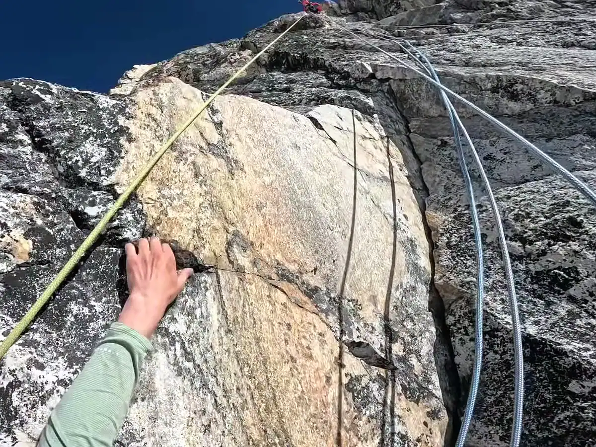 POV of a rock climber gripping a steep granite cliff face with climbing ropes on a mountain ascent.